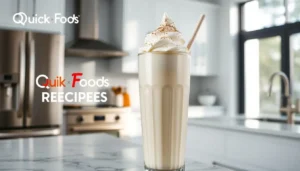 Tall glass of creamy vanilla milkshake with whipped cream topping in a modern kitchen.